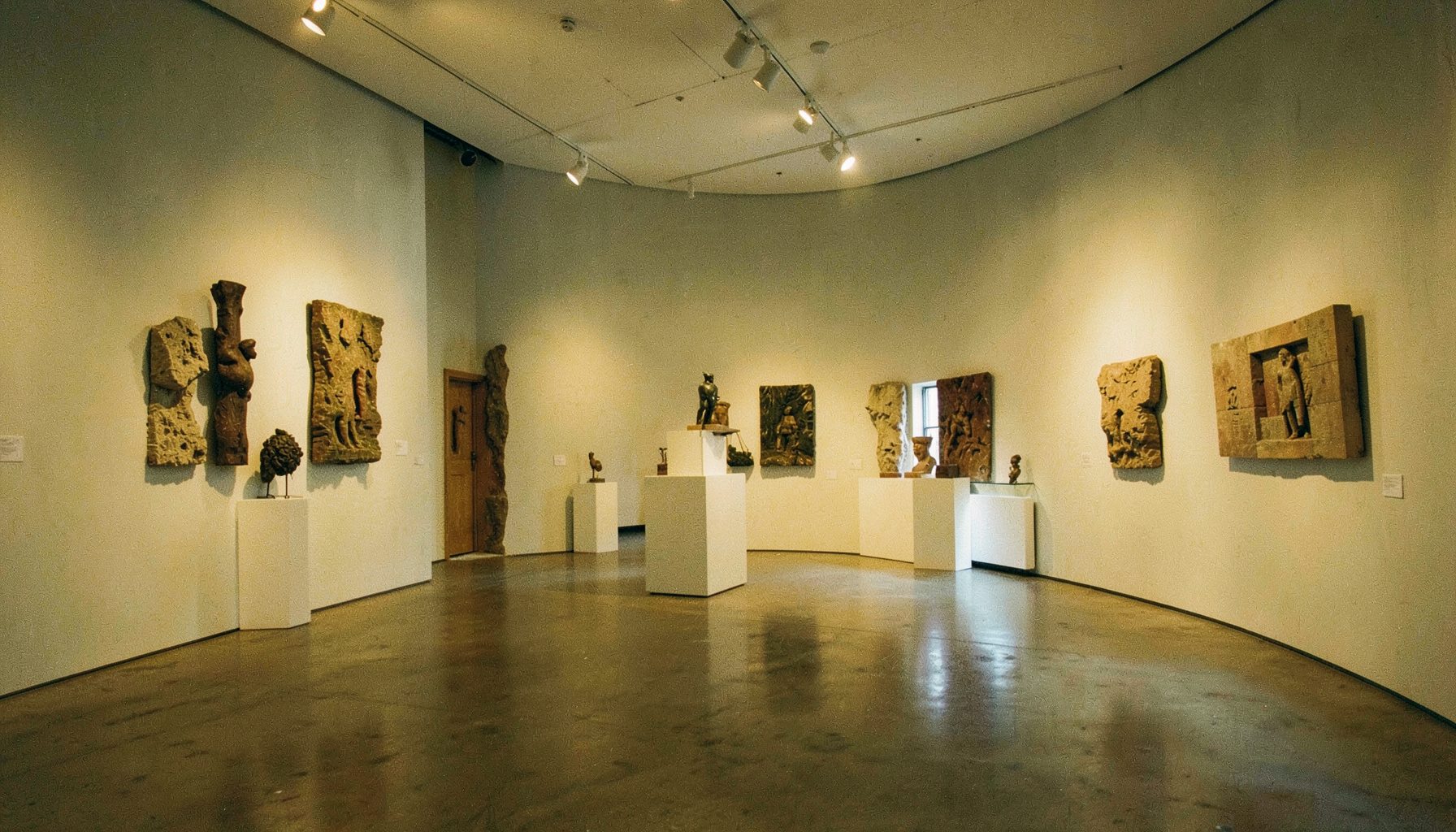 An art gallery interior with sculptural elements and soft gallery lighting, muted grays and warm earth tones filling the room